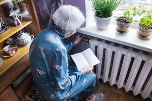 The senior woman holding gas bill in front of heating radiator. Payment for heating in winter.